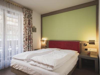 Helles Hotelzimmer mit Doppelbett, grünem Akzent an der Wand und Vorhängen am Fenster.