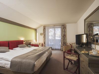Hell eingerichtetes Hotelzimmer mit Doppelbett, Fernseher, Schreibtisch und Zugang zu einem Balkon.