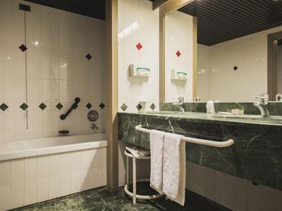 Modernes Badezimmer mit Badewanne, Waschbecken aus grünem Marmor und weißen Fliesen mit Akzenten.