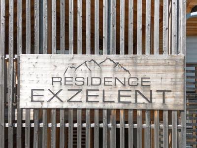 Schild mit der Aufschrift "Residence Exzellent" vor vertikalen Holzbalken.