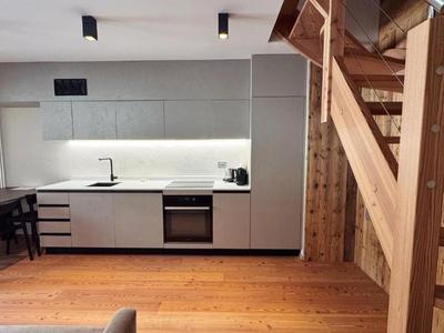 Moderne Küche mit weißen und grauen Schränken neben einer Holztreppe in einer Hotelunterkunft.