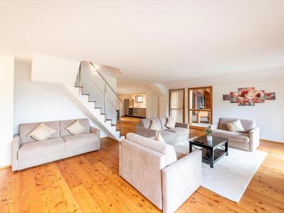 Großzügiges Wohnzimmer mit modernen Sofas, Holzboden, Treppe und hellem, offenem Raum.