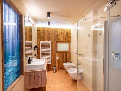 Helles Badezimmer mit Holzverkleidung, Waschbecken, WC, Bidet und Dusche, Fenster mit Vorhang.