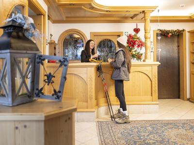 Hotelrezeption mit einem Mädchen, das mit dem Personal spricht, warme Holzmöbel und dekorative Laternen.