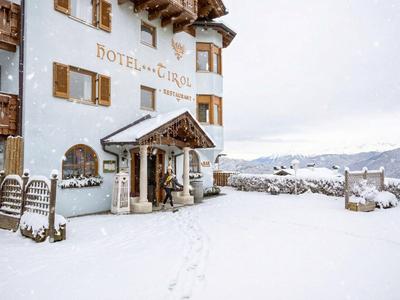 Schneebedecktes Hotel mit Holzbalkonen und Bergblick bei bewölktem Himmel.