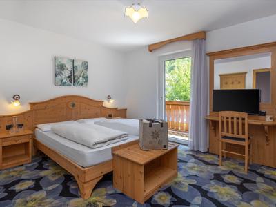 Hell eingerichtetes Hotelzimmer mit Holzmöbeln und Balkon mit grüner Aussicht.