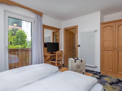 Hell eingerichtetes Hotelzimmer mit zwei Betten, Holzmöbeln und Balkon mit Blick auf grüne Bäume.