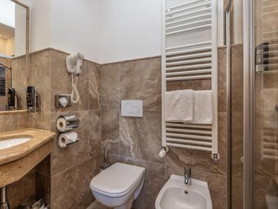 Kompaktes Badezimmer mit Toilette, Bidet, Waschbecken und Handtuchheizung in neutralen Braun- und Beigetönen.