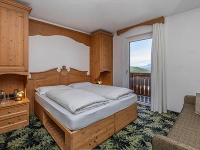 Gemütliches Hotelzimmer mit Holzmöbeln, Doppelbett, Balkon und gemütlichem Teppichboden.