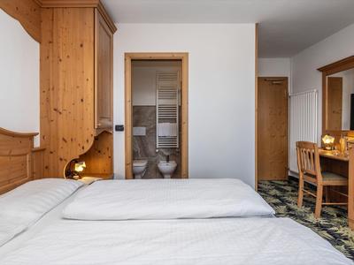 Helles Hotelzimmer mit Doppelbett, Holzmöbeln und einem modernen Bad sichtbar durch eine Glastür.