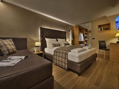 Modernes Hotelzimmer mit großem Bett, Sofa und Holzboden in warmen Brauntönen.