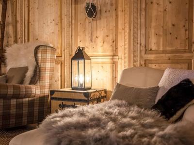 Gemütliches Hotelzimmer mit Holzverkleidung, Sessel, Sofa und beleuchtetem Laternenlicht.