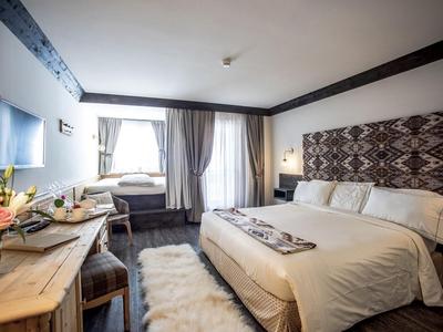 Modern eingerichtetes Hotelzimmer mit zwei Betten, Holzmöbeln und Vorhängen an der großen Fensterfront.