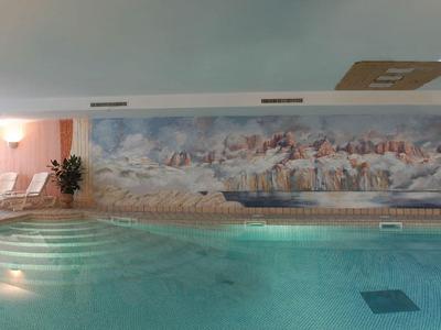 Innenhotelpool mit großen Fenstern und Wandmalerei einer Küstenlandschaft.