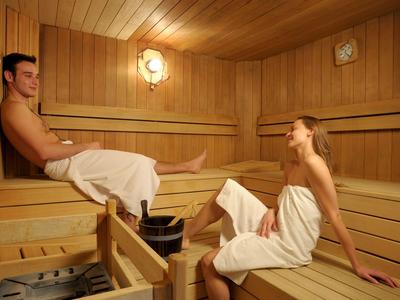 Zwei Personen entspannen in einer Holzsauna, jede mit einem weißen Handtuch bedeckt.