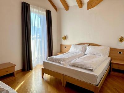 Helles Hotelzimmer mit Holzbett, Nachttischen, Vorhängen und Holzbalken an der Decke.