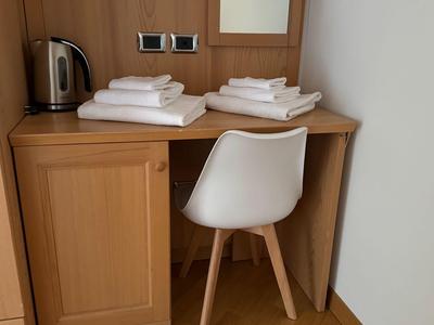 Kleiner Hotelarbeitsplatz mit Holzschreibtisch, weißem Stuhl, Wasserkocher und gefalteten Handtüchern.