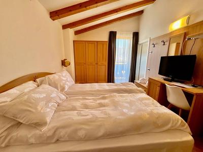 Gemütliches Hotelzimmer mit Doppelbett, Schrank und Schreibtisch unter sichtbaren Holzbalken.