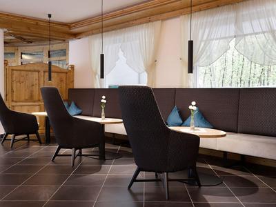 Gemütliche Sitzecke mit schwarzen Sesseln, brauner Polsterecke und Holzdecke in einem Hotel.