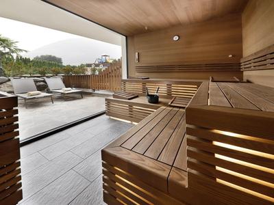 Moderne Holzsauna mit Blick auf Terrasse und Liegestühle im Freien.