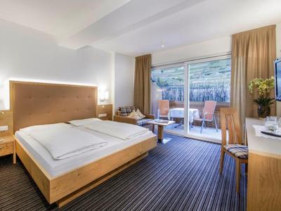 Modernes Hotelzimmer mit Doppelbett, Balkon, TV und Holzmöbeln in neutralen Farben.