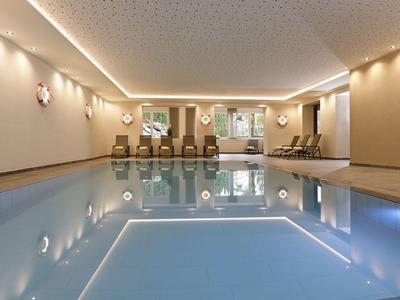 Helles Hallenbad mit Liegestühlen und gedämpfter Beleuchtung in einem Hotel.