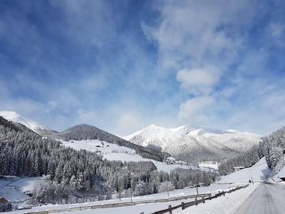 Verschneite Berglandschaft mit klar blauem Himmel und bewaldeten Hängen, ideal für Winterurlaub.
