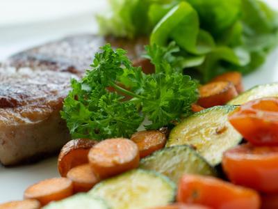 Gegrilltes Steak mit gebratenem Gemüse und frischen Salatblättern auf weißem Teller.