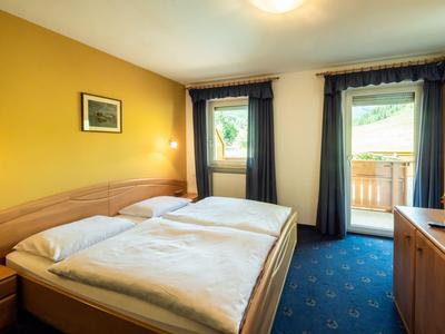 Ein helles Hotelzimmer mit Doppelbett, gelber Wand und Balkonblick.