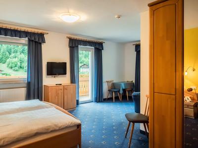 Hell eingerichtetes Hotelzimmer mit großen Fenstern, blauen Vorhängen und Teppichboden.