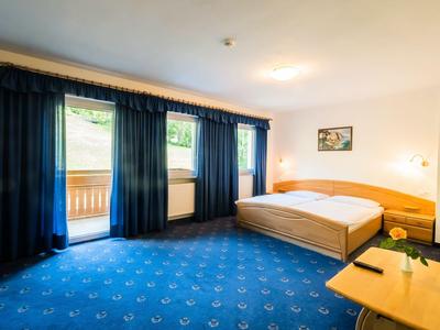 Helles Hotelzimmer mit großem Bett, dunkelblauen Gardinen und Teppichboden.
