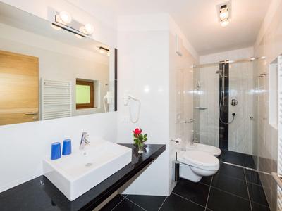 Modernes Badezimmer mit weißem Waschbecken, Glasdusche und schwarzen Bodenfliesen.