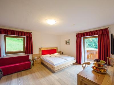 Helles Hotelzimmer mit Doppelbett, roten Vorhängen und Zugang zu einem Balkon mit Bergblick.