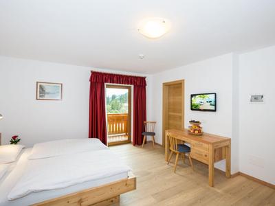 Helles Hotelzimmer mit Doppelbett, Holzmöbeln und Balkon mit rotem Vorhang.