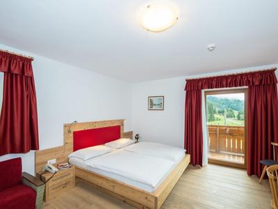 Helles Hotelzimmer mit Doppelbett, roten Vorhängen und Balkon mit Blick ins Grüne.