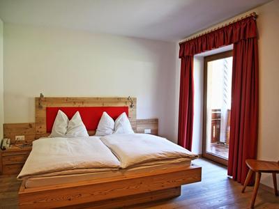 Helles Hotelzimmer mit Holzbett, roten Akzenten und Balkon mit Blick nach draußen.