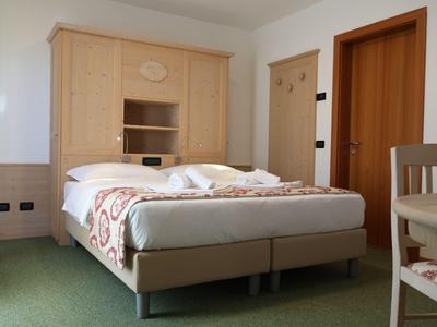 Hell eingerichtetes Hotelzimmer mit Doppelbett, Holzschrank und grünem Teppichboden.