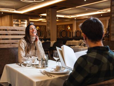 Dos personas sentadas en una mesa puesta en un restaurante, la mujer se ríe.