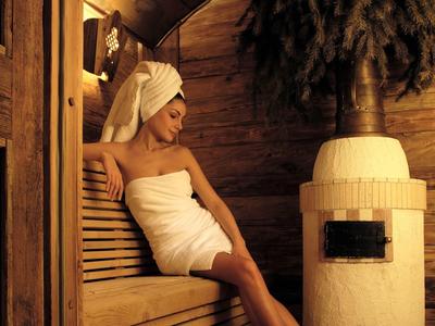 Mujer relajándose en sauna de madera envuelta en toalla y turbante en la cabeza.