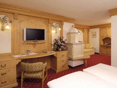 Habitación de hotel con cama doble, muebles de madera, escritorio, TV y estufa en tonos cálidos.