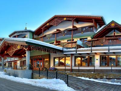 Gran edificio de hotel estilo alpino con detalles de madera y nieve en primer plano.