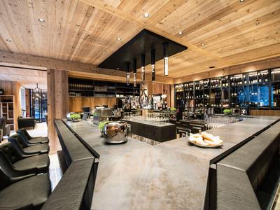 Moderne Hotelbar mit Holzboden, Theke, Sitzgelegenheiten und beleuchteten Regalen.