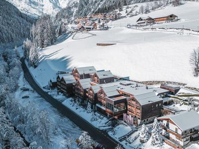 Winterliche Berglandschaft mit verschneiten Chalets in einem Tal neben einer Straße.