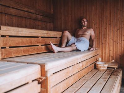 Mann entspannt in einer hölzernen Sauna mit Handtuch und Sauna-Eimer.