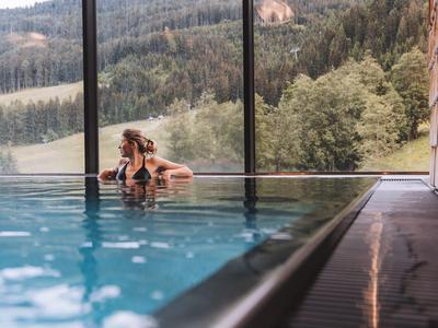 Frau entspannt im Infinity-Pool mit Blick auf bewaldete Hügel und Berge.