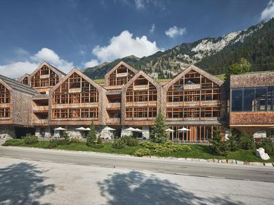 Modernes Hotelgebäude aus Holz mit großen Fenstern vor Bergkulisse und sonnigem Himmel.