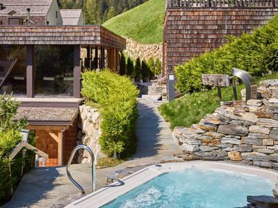 Außenbereich eines Hotels mit Whirlpool, Steinmauern und grünen Hügeln im Hintergrund.