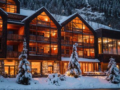 Modernes Hotel mit großen Glasfenstern und beleuchteten Zimmern im verschneiten Winterwald.