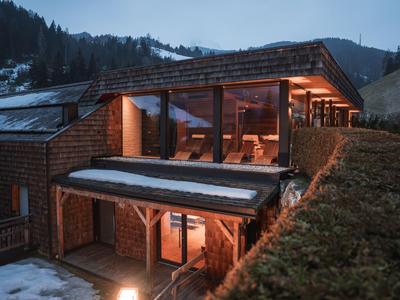 Modernes Berghotel mit Holzfassade und großen Fenstern in verschneiter Landschaft bei Dämmerung.