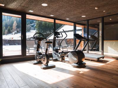 Modernes Fitnessstudio mit Ergometern und Laufband vor großen Fenstern mit Bergblick.